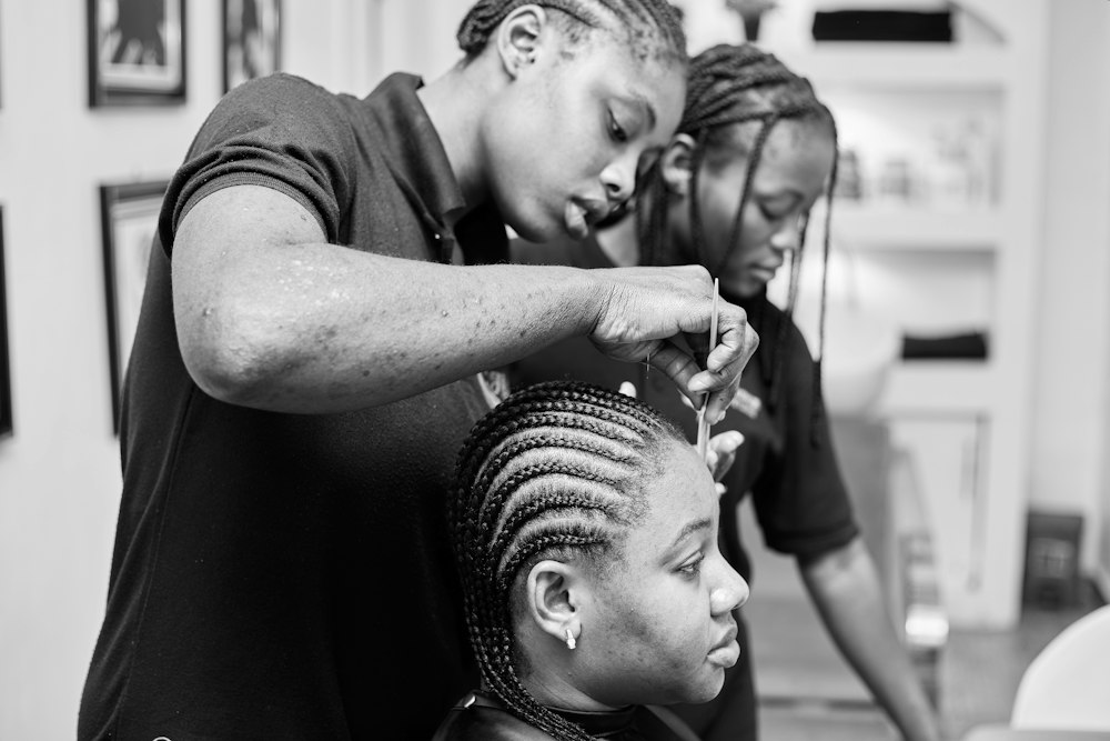 Dos estilistas trenzando el cabello de una clienta, foto de referencia